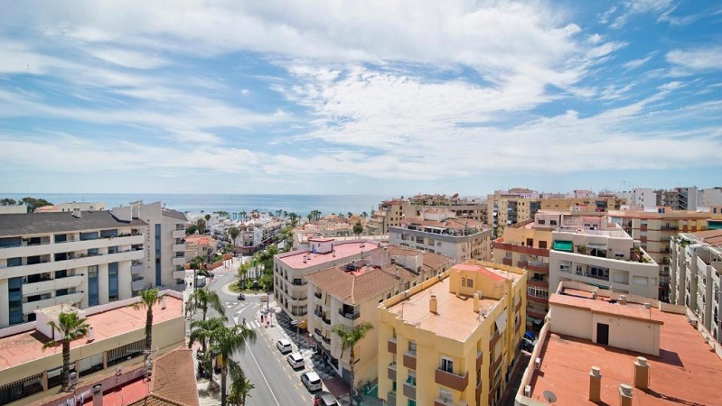 Almuñécars stadsvy med palmkantade gator, färgglada tak och Medelhavet i horisonten under en solig himmel med vita moln.