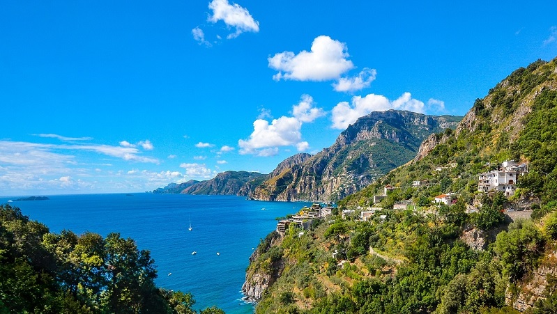 Amalfikusten Dramatisk kustlinje längs Amalfikusten med branta klippor, blått hav och pittoreska hus på bergssidan.