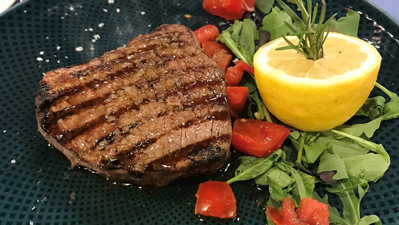 Grillad köttbit med citron, ruccola och tomater på svart tallrik - en färgstark och aptitretande måltid.