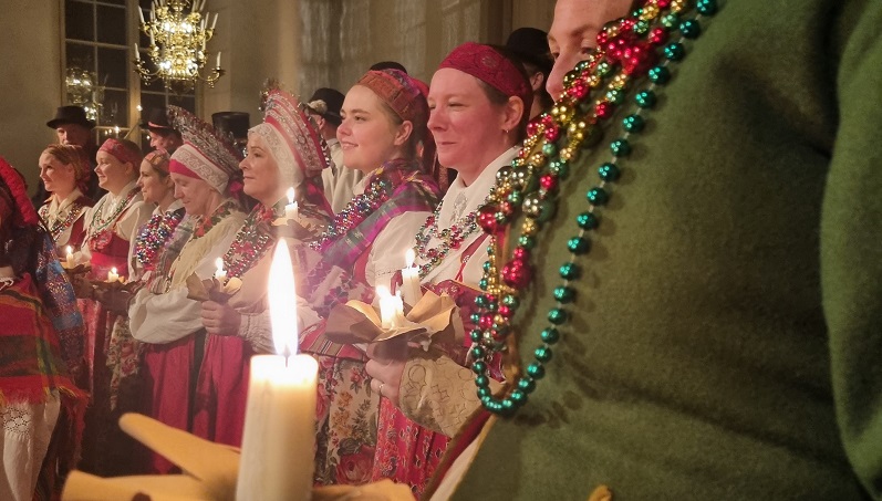 Konserten Dalarnas Lussibrud Sångare klädda i vita, röda och gröna folkdräkter. Stämningsfullt ljus brinner.