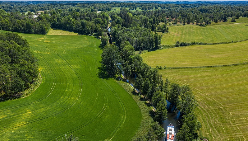 Kinda kanal Bild: Visit Linköping & Co, Fredrik Schlyter Drönarbild som visar en båt som åker fram på Kinda kanal med grönt landskap runt omkring
