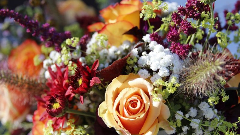 Färgstark blombukett med rosor, brudslöja och vilda blommor i olika nyanser av orange, vitt, lila och grönt.