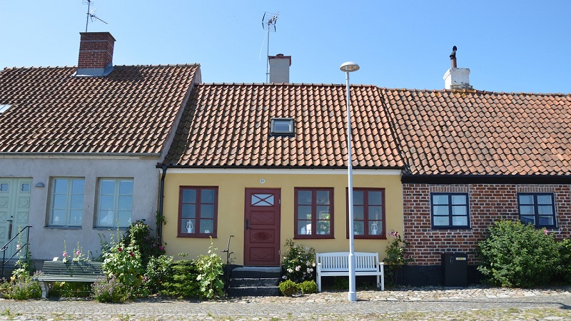 Simrishamn Färgglada husfasader med tegel- och putsade väggar i Simrishamn, blommor och bänk framför kullerstensgata.