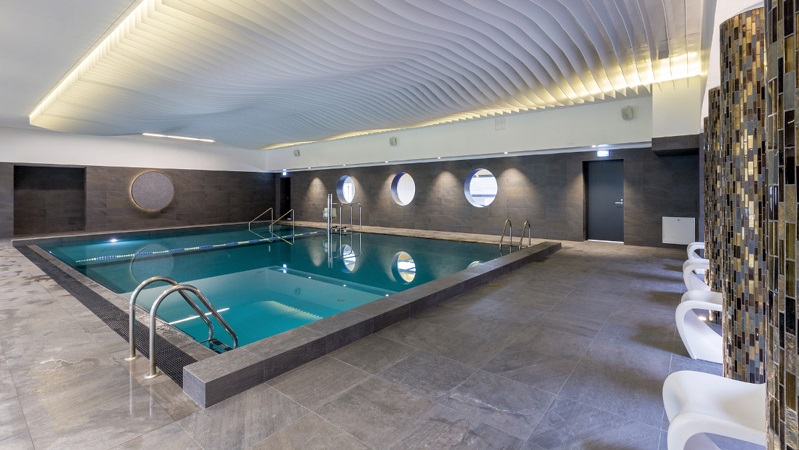 Modern inomhuspool med stilren design, rundade fönster, dämpad belysning och avkopplande atmosfär.